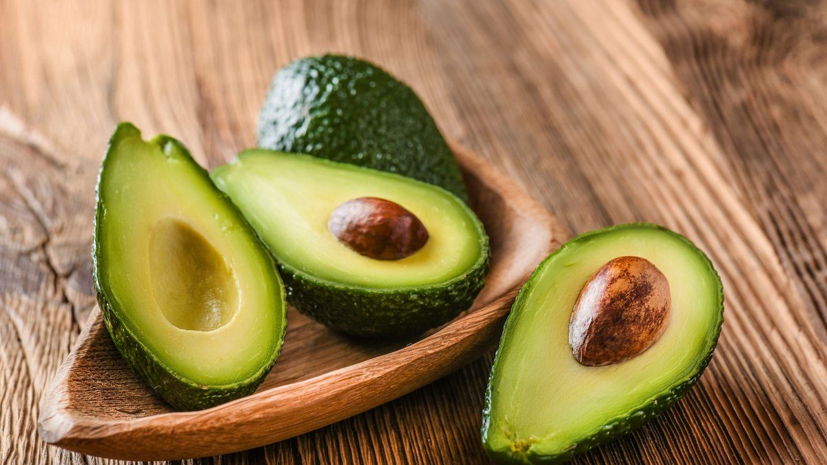 Fresh avocados halved on a wooden platter